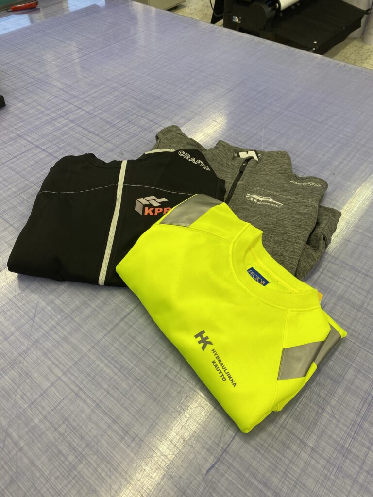 Logopaidat kolme työvaatetta pöydällä